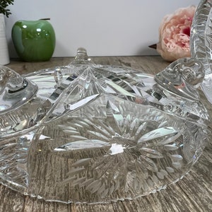 Puede incluir: Un cuenco de vidrio transparente con un dise&ntilde;o de cristal tallado. El cuenco tiene tres patas y un borde festoneado.