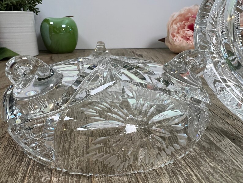 Puede incluir: Un cuenco de vidrio transparente con un dise&ntilde;o de cristal tallado. El cuenco tiene tres patas y un borde festoneado.