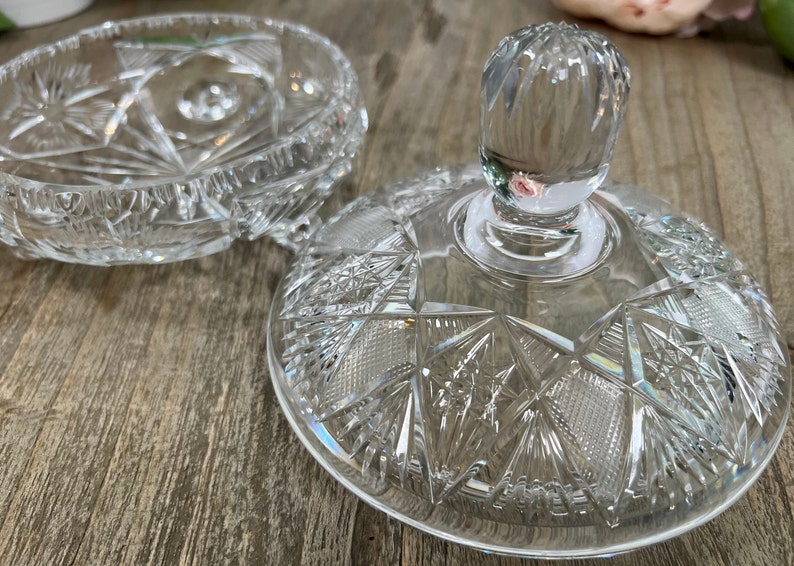 Puede incluir: Un plato de vidrio transparente con tapa, decorado con un dise&ntilde;o de vidrio cortado. La tapa tiene un pomo en la parte superior.
