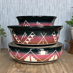 May include: Set of three black ceramic bowls with a southwestern design. The bowls feature a gradient of red, orange, and brown colors with white geometric patterns.