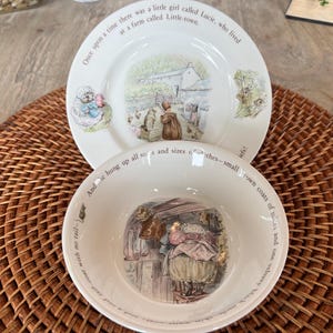 May include: A white ceramic plate and bowl set with illustrations and text. The plate features a farm scene and the text "Once upon a time there was a little girl called Lucie, who lived at a farm called Little-town."