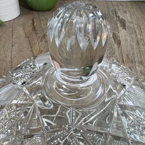 Puede incluir: Una tapa de cristal transparente con un dise&ntilde;o de cristal tallado. La tapa tiene un pomo redondo en la parte superior.