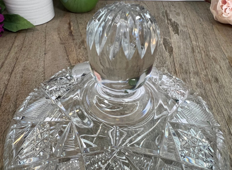 Puede incluir: Una tapa de cristal transparente con un dise&ntilde;o de cristal tallado. La tapa tiene un pomo redondo en la parte superior.