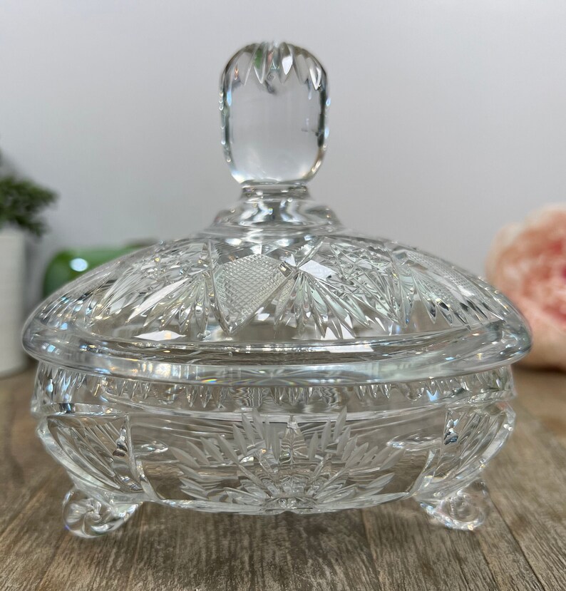 Puede incluir: Un platito de cristal transparente para dulces con tapa. El plato tiene un dise&ntilde;o de cristal tallado y se apoya en tres patas. La tapa tiene un pomo en la parte superior.