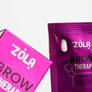Peut inclure: Un sachet rose et blanc de Zola Brow Therapy, un produit pour les sourcils et les cils. Le sachet est étiqueté avec le nom du produit et le texte "BROWS & LASH RESTRUCTURING MEMBRANE-LIFE COMPLEX". Le sachet comprend également le texte "1.5 ml MADE IN UKRAINE".