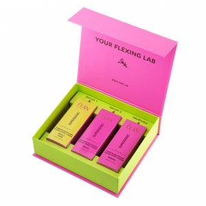 Puede incluir: Una caja rosa con el texto "YOUR FLEXING LAB" y "elan.net.ua" en la tapa. La caja está abierta y contiene tres frascos de suero etiquetados como "ÉLAN SUPERSONIC" con el texto "Serum 1", "Serum 2" y "Multivitor" en los frascos.