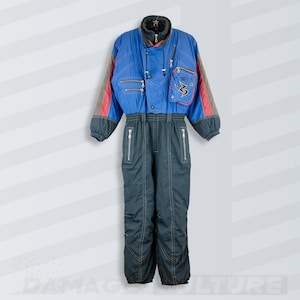 Può includere: Una tuta da sci vintage blu e nera con accenti rossi e grigi. La tuta intera presenta più tasche con cerniera, un colletto alto e un emblema decorativo sul petto. Progettata per attività con tempo freddo.