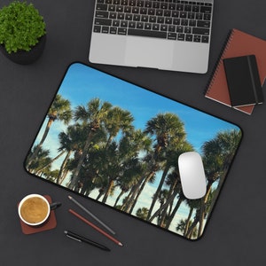 May include: A blue and green palm tree design mousepad with a white computer mouse on top. The mousepad is on a black surface.