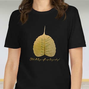 Könnte beinhalten: Schwarzes T-Shirt mit einem goldenen Blattdruck mit den Worten "Richtige Konzentration", "Richtige Achtsamkeit", "Richtige Anstrengung", "Richtige Sprache", "Richtiges Handeln", "Richtiger Lebensunterhalt", "Richtige Absicht", "Richtige Sicht", und "Kultiviere mit all deiner Kraft, übermenschliche Stärke ist in dir!"