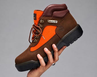 May include: A brown and orange ankle boot featuring a dark brown padded collar, brown suede-like panels, and bright orange fabric side inserts. The boot has a black lug sole, brown laces, gold-tone metal eyelets, and a Timberland logo tag.