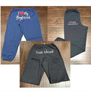 May include: Three pairs of black sweatpants with different text printed on the back. One pair says "I love my boyfriend", another says "I love my girlfriend", and the last pair says "Team Edward".