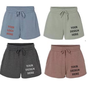 May include: Four pairs of women's shorts in different colors: light blue, green, gray, and pink. Each pair has a drawstring waistband and a pocket on each side. The shorts have text printed on them that says "Your Logo Here" or "Your Design Here".