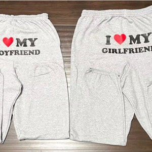 May include: Two pairs of gray sweatpants with black text and a red heart. One pair says "I love my boyfriend" and the other says "I love my girlfriend".