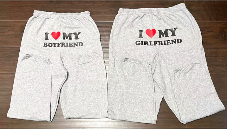 May include: Two pairs of gray sweatpants with black text and a red heart. One pair says "I love my boyfriend" and the other says "I love my girlfriend".