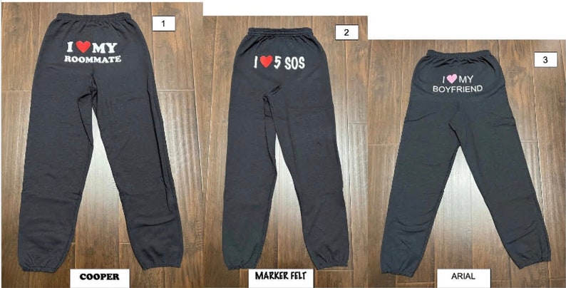 May include: Three pairs of dark gray sweatpants with different text printed on the back. The first pair says "I love my roommate" with a red heart. The second pair says "I love 5 SOS" with a red heart. The third pair says "I love my boyfriend" with a pink heart.