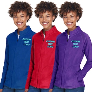 May include: Three zip-up fleece jackets in royal blue, red, and purple. Each jacket features a high collar, long sleeves, and the text CUSTOM TEXT LOGO printed in light blue on the left chest area. The jackets are shown in a side-by-side arrangement.