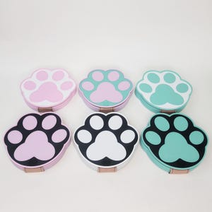 May include: Six colorful paw print coasters. The coasters are made of silicone and have a black rim. The paw prints are in pink, white, and green.