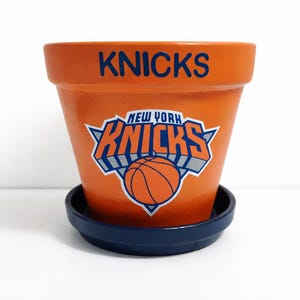 May include: A white ceramic mug with a black handle and the text "But First, Coffee" in a black, handwritten-style font. The mug is on a white surface.