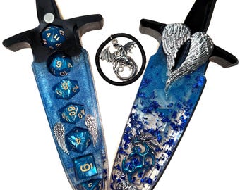 May include: Two decorative dagger-shaped objects with black handles and blue resin blades. The blades are embedded with blue dice and silver wing accents. A circular charm with a dragon is between the daggers.