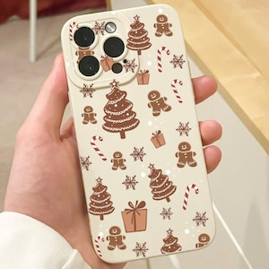 May include: A beige phone case featuring a repeating pattern of brown Christmas trees, gingerbread men, candy canes, snowflakes, and gift boxes. The case has a camera cutout.