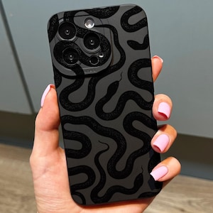 以下が含まれることがあります： 黒いスマートフォンケース。黒いヘビの繰り返し模様が特徴です。ケースはマット仕上げで、スマートフォンの背面と側面を覆い、カメラレンズとボタン用の切り欠きがあります。