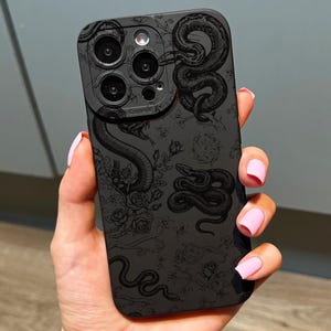 May include: Black smartphone case with a detailed snake design. The case has a matte finish and includes a camera lens protector. The snake artwork is intricately detailed, with floral accents. The case is designed for a smartphone.