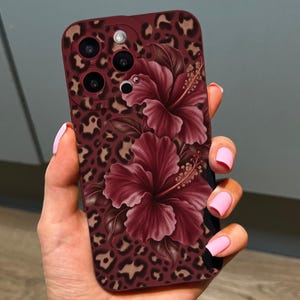 May include: A smartphone case featuring a dark red and brown leopard print pattern overlaid with two large, deep red hibiscus flowers. The case includes cutouts for a triple camera system and a flash, showcasing a detailed floral and animal print design.