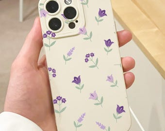 May include: A cream-colored phone case adorned with a repeating pattern of purple flowers and green leaves. The case has a camera cutout with a raised edge. The overall design is floral and delicate.