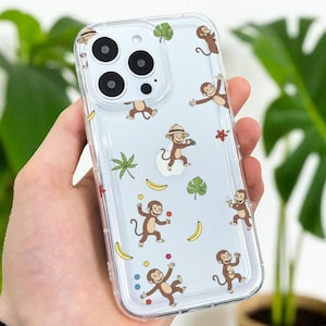 May include: Transparent phone case decorated with a fun monkey design. The case shows cartoon monkeys in different poses, with bananas, leaves, and flowers. The design is set against a light blue background.