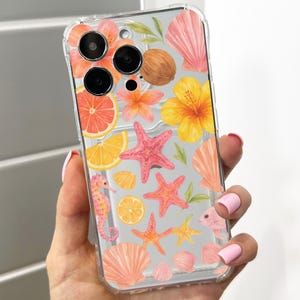 Op de afbeelding: Transparante telefoonhoes met een tropisch ontwerp. Het heeft aquarel illustraties van zeesterren, schelpen, hibiscusbloemen en citrusvruchten. De hoes wordt in een hand gehouden, waarbij de levendige kleuren en het strandthema worden getoond.