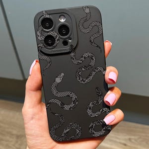 May include: A black smartphone case with a repeating pattern of grey snakes. The case has a matte finish and a camera cutout. The snakes are illustrated with detailed scales and heads. The case is designed for a mobile phone.