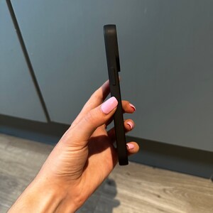 May include: A black phone case with a raised camera bump. The case is made of a smooth, matte material.