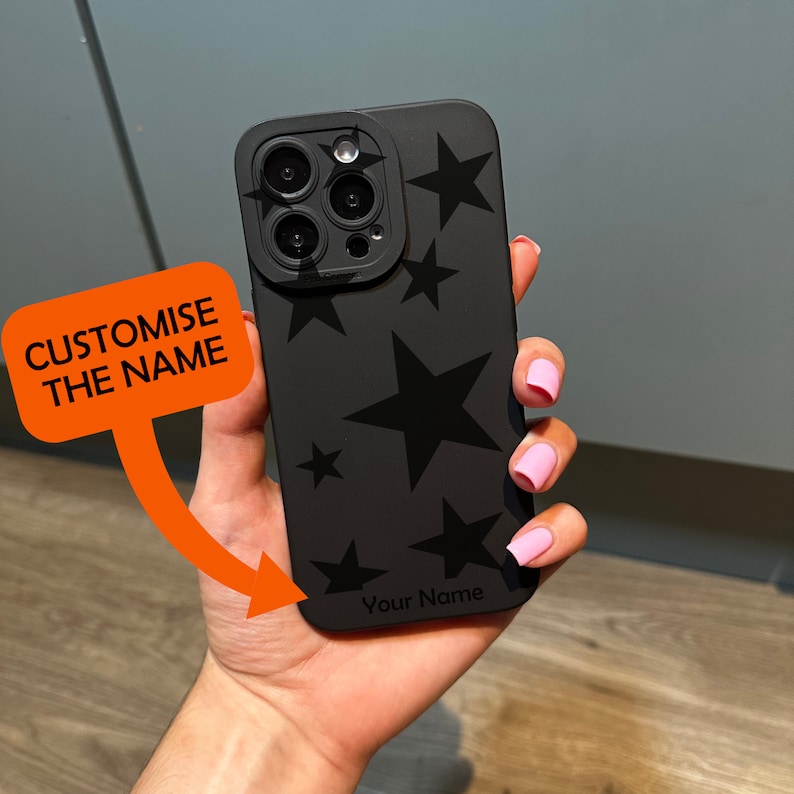 May include: Black phone case with a black star pattern and a clear camera lens cover. The case has the text "Your Name" printed on the bottom.