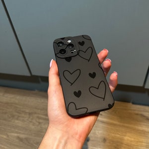 May include: A black phone case with a pattern of black hearts. The case has a camera lens cutout.