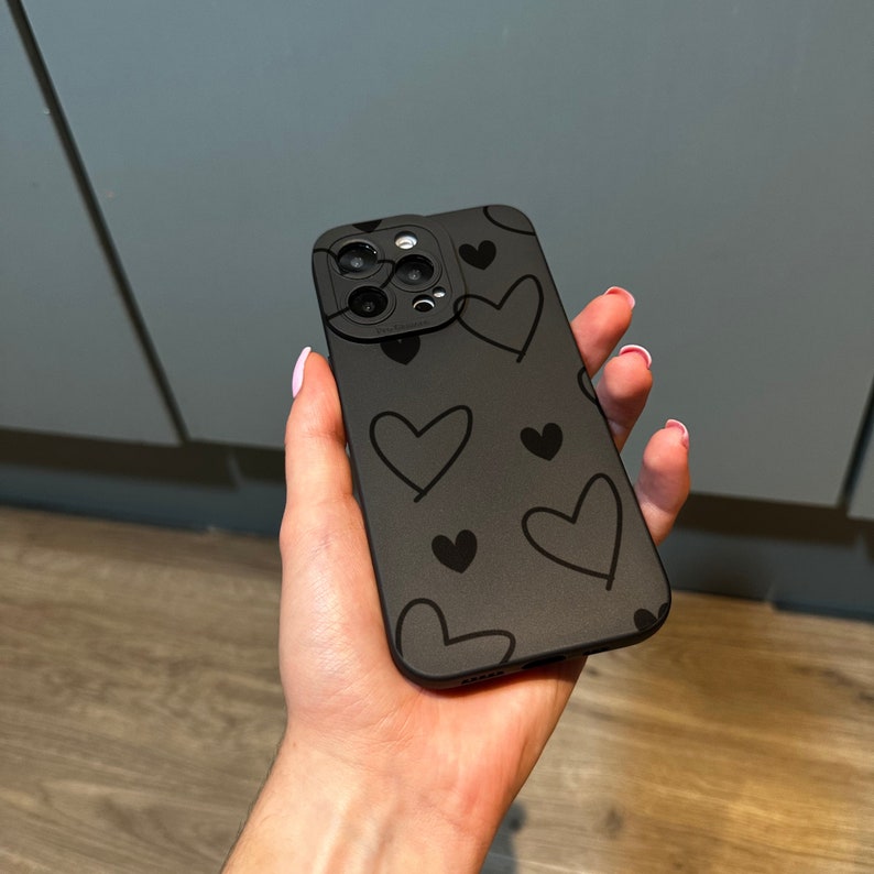 May include: A black phone case with a pattern of black hearts. The case has a camera lens cutout.