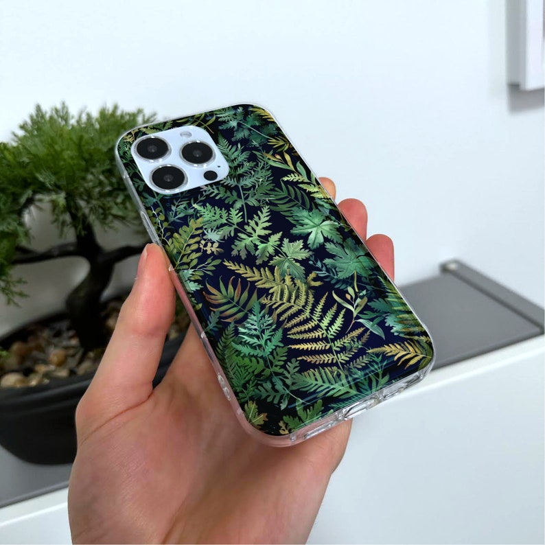 May include: A clear phone case with a green and gold fern pattern. The case is designed for an iPhone.