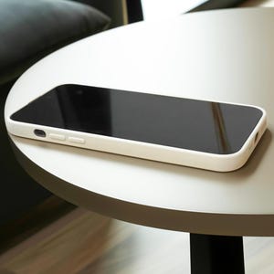 May include: A white smartphone case with a black screen is lying on a light gray table.
