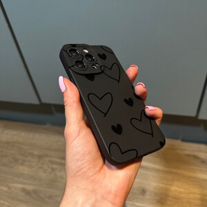 May include: Black phone case with a pattern of small black hearts on a black background. The case has a raised camera lens cover.