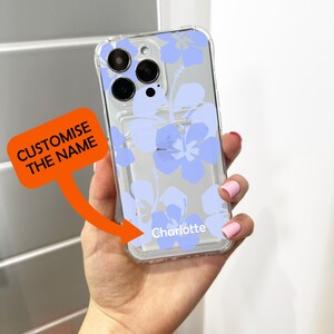 May include: A clear phone case with a blue floral design. The case has a cutout for the camera lens and a space for a name. The name "Charlotte" is printed on the case.