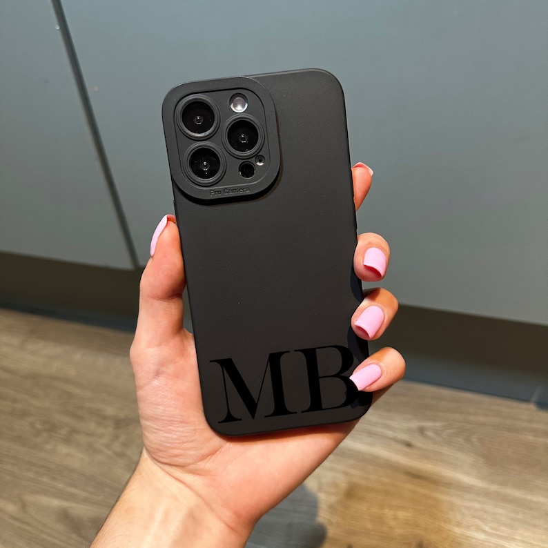 May include: Black phone case with a camera lens cover and the initials "MB" printed on the back.