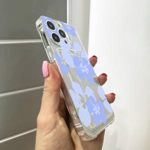May include: A clear phone case with a light blue floral design. The case is designed for a smartphone with a triple lens camera.