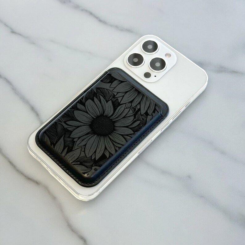 May include: A white iPhone with a black floral phone wallet attached to the back.