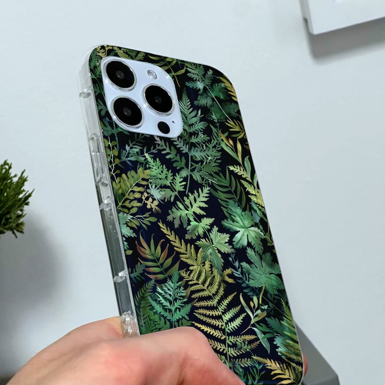 May include: A clear phone case with a green and gold fern pattern. The case is designed for an iPhone.