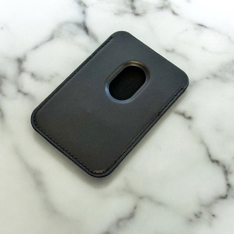 May include: A black leather card holder with a stitched edge and a cut-out for a card.