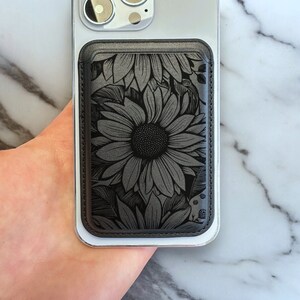 May include: Black leather phone case with a sunflower design. The case has a stitched edge and a cutout for the camera lens.
