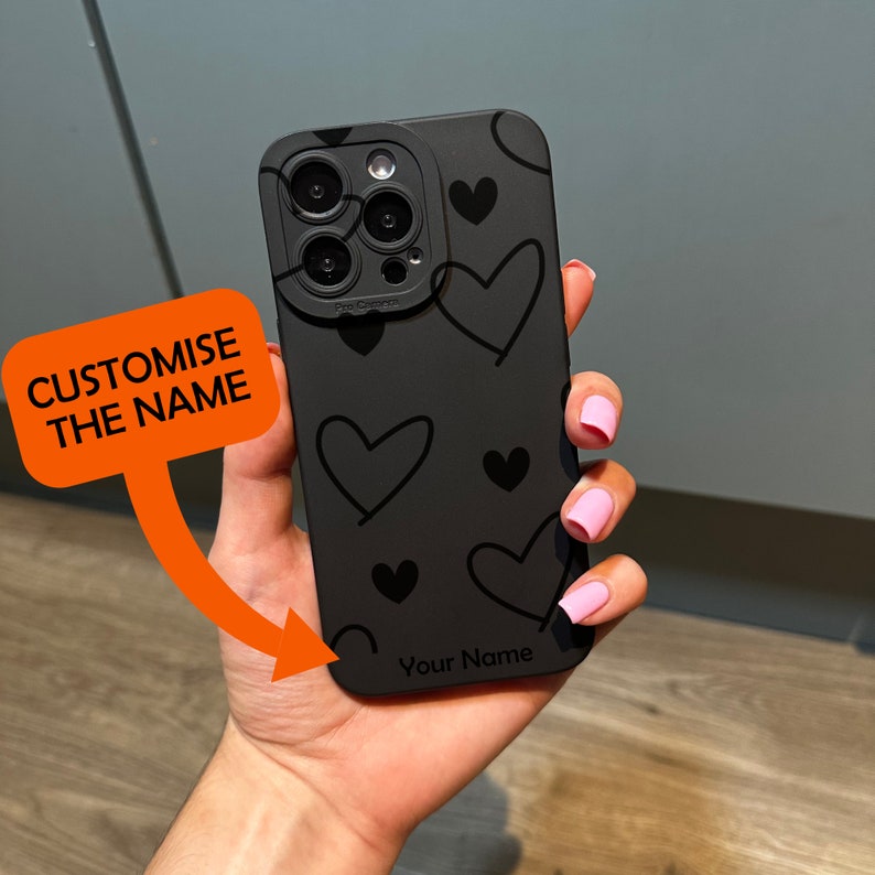 May include: Black phone case with a heart pattern and a camera lens cover. The case has the text "Your Name" printed on the bottom.