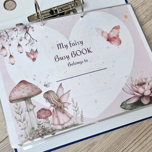May include: A pink and white heart-shaped page with the text "My fairy Busy BOOK Belongs to" and illustrations of a fairy, mushrooms, a butterfly, and a water lily.