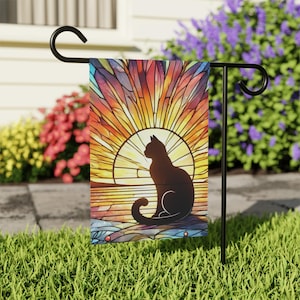 May include: A black cat silhouette sits in front of a stained glass sunset. The sunset is a vibrant mix of orange, yellow, red, and purple. The cat is facing left and has a long tail.
