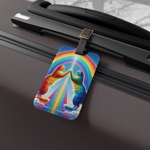 May include: A luggage tag featuring two cats with rainbow fur, pawing at each other in front of a rainbow. The cats are on a white cloud with a rainbow beam of light shining down on them.