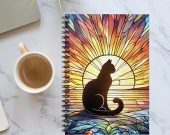 May include: A spiral bound notebook with a colorful stained glass design featuring a black silhouette of a cat sitting in front of a sunset.